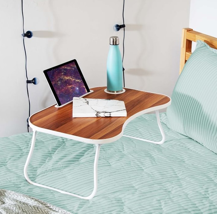 Foldable lap desk with tablet and book on bed