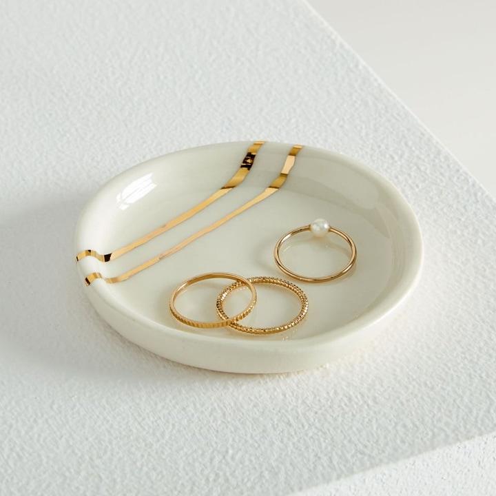 White and gold ring dish holding three rings.