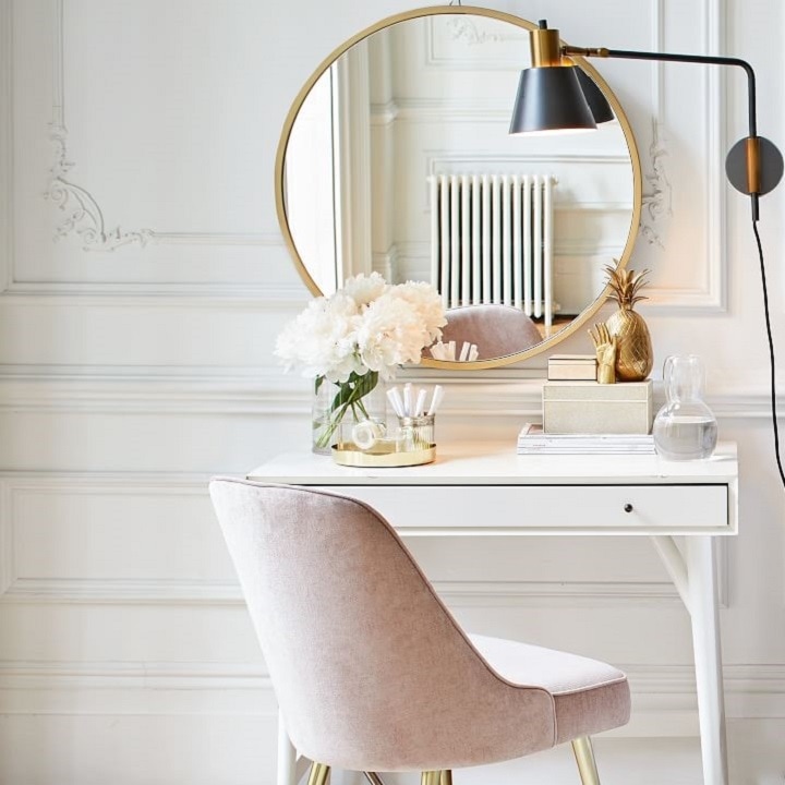 Small white desk with pink chair and gold round mirror.