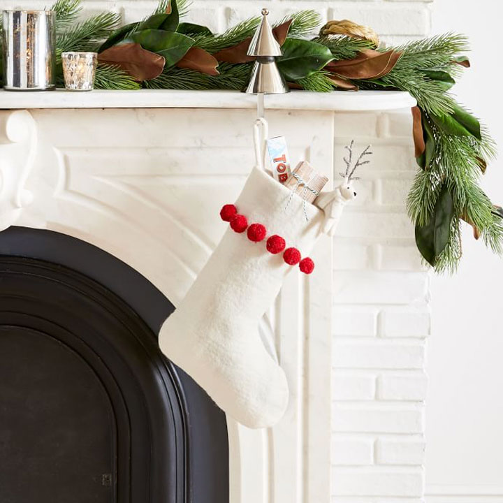 white felt stocking with red pom poms hung from a fireplace 