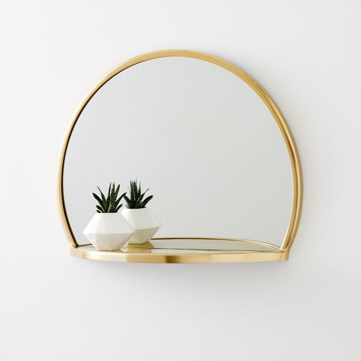 Rounded gold mirror hanging on a wall with small plant