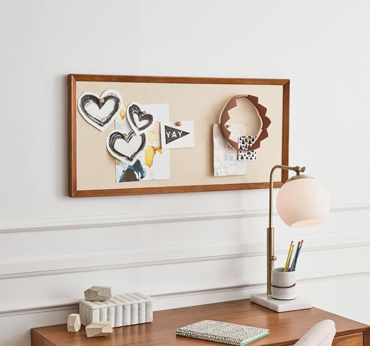 Wood-framed pinboard with artwork above desk.