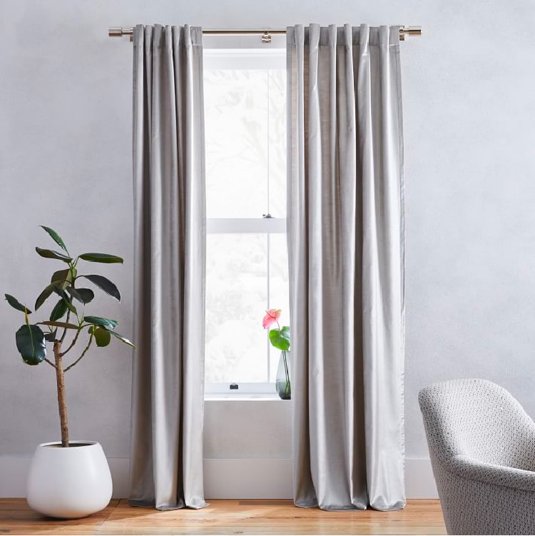 Curtains hanging from window with large plant and armchair