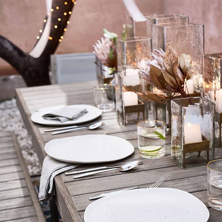 Glass and brass candle holders on wooden, plated table.