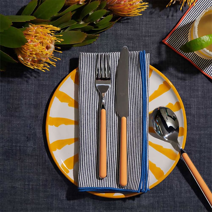 Yellow patterned plate and utensils with blue striped napkin.