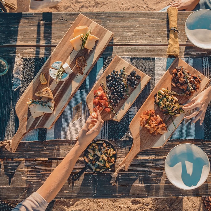 Three wooden serving planks with food on wooden table.