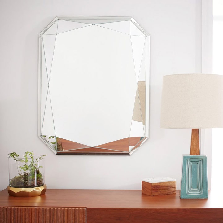 Mirror hanging above cabinet with table lamp and plant.