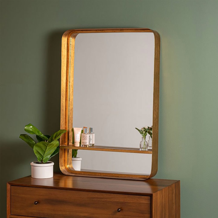 Mirror with shelf above dresser leaning against wall.