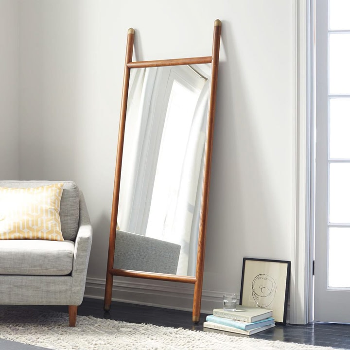 Floor length mirror leaning against wall next to armchair.