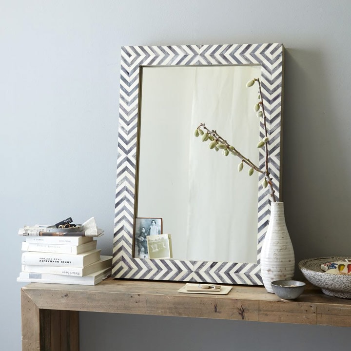 Herringbone mirror on top of table with books and vase.