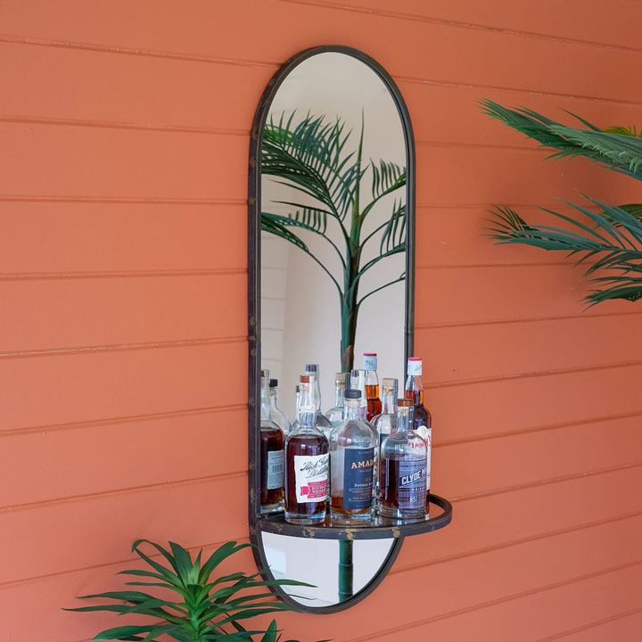 Oval mirror with shelf holding liquor bottles.