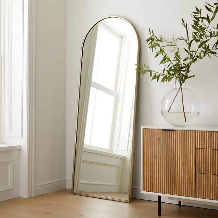 Arched floor mirror leaning against wall next to cabinet.