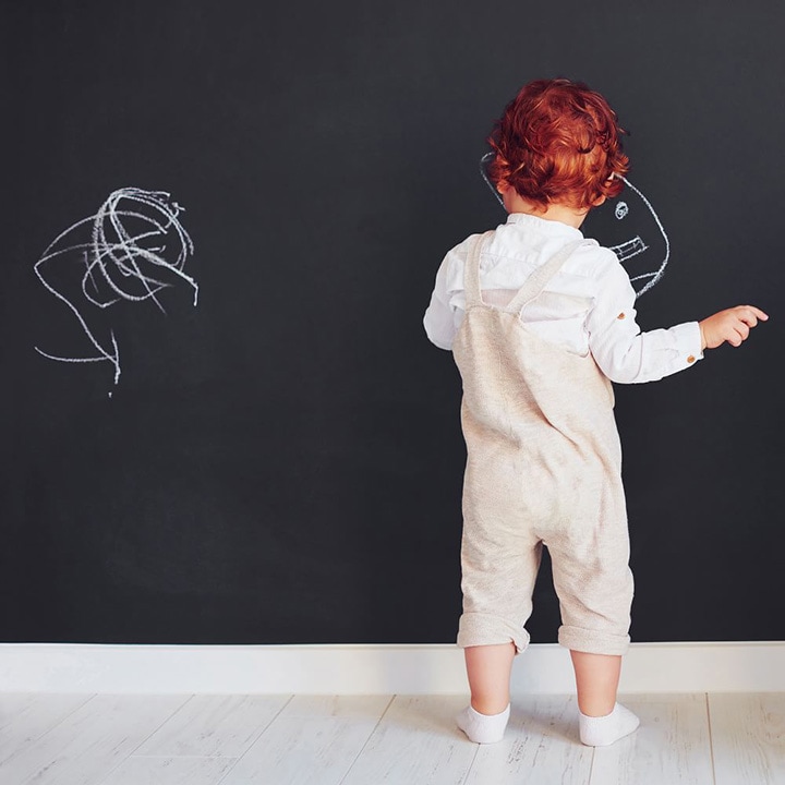 Child drawing on black chalkboard wall