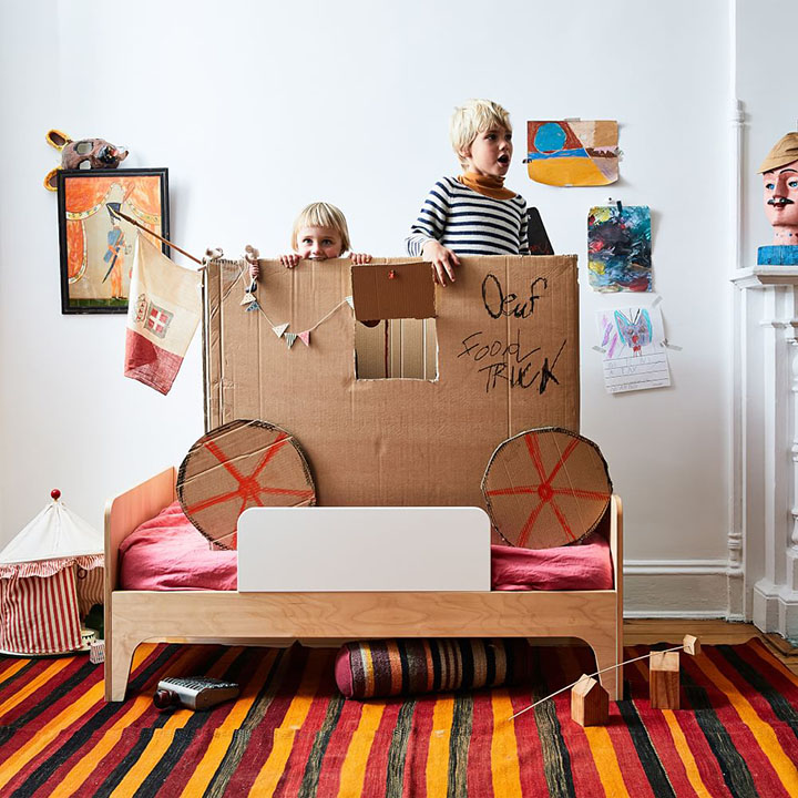 Two children standing behind a play food truck crafted from cardboard