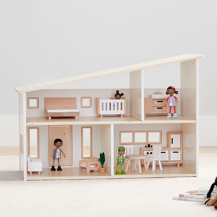 Angular wooden dollhouse with four rooms and four dolls placed inside