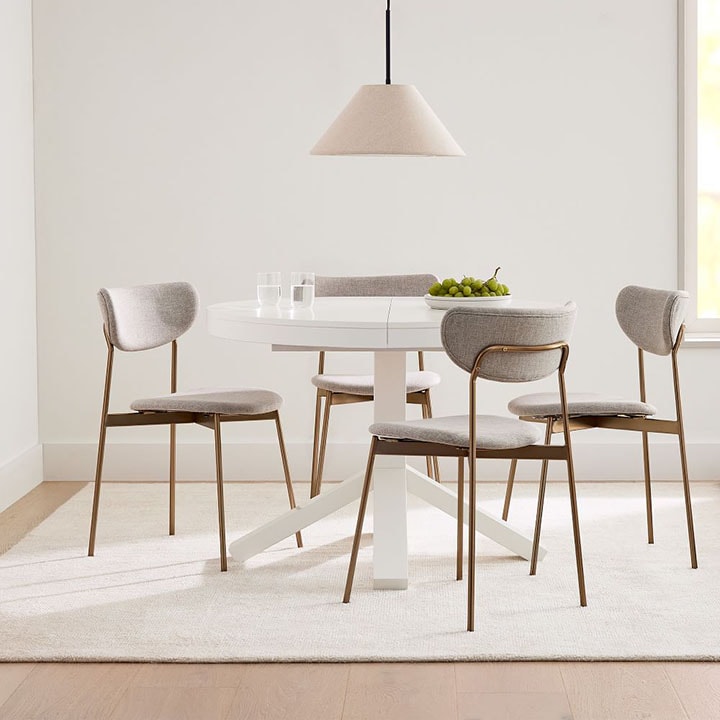 White expandable dining table with white overhead light and bronze dining chairs. 