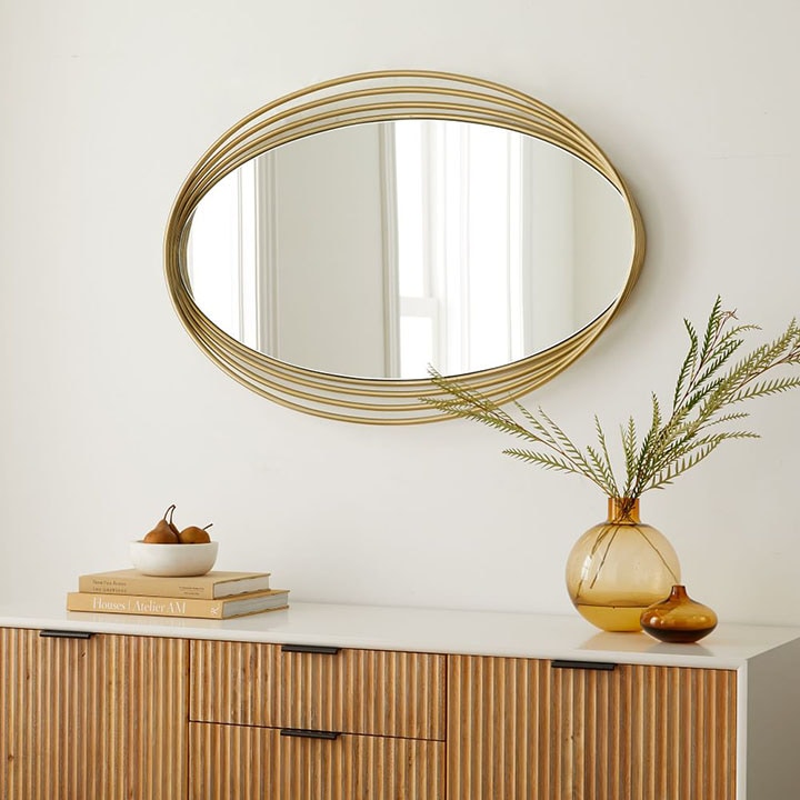 Gold oval mirror on white wall above mid-century modern console table.