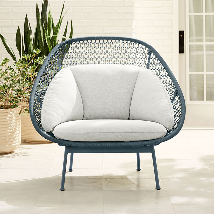 Blue gray nest chair with neutral cushion next to outdoor plant. 