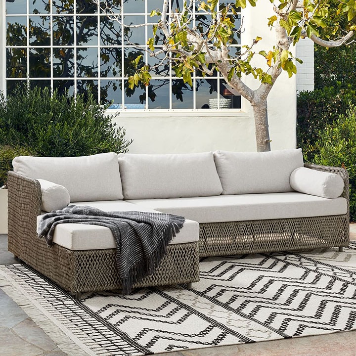 Wicker chaise sectional with dark throw blanket and zig-zag rug. 