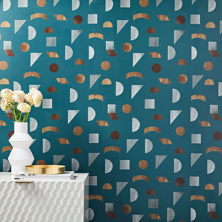 Teal blue wallpaper with geometric shapes behind white media table and white vase.