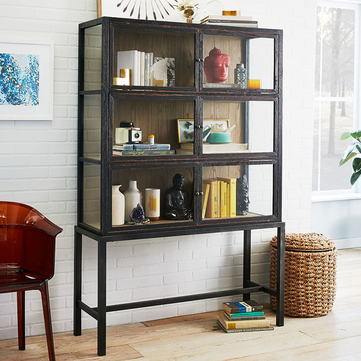 Bookcase display case with organized decorative objects and books next to window. 