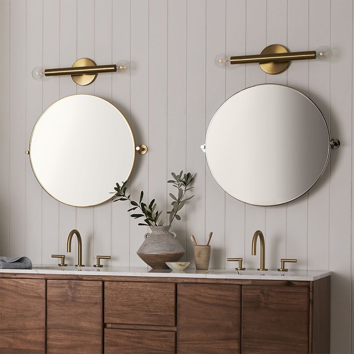 Two tubular sconces mounted over round bathroom mirrors.