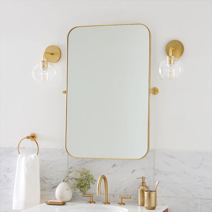 Matching brass sconces with round glass shades on either side of a mirror.