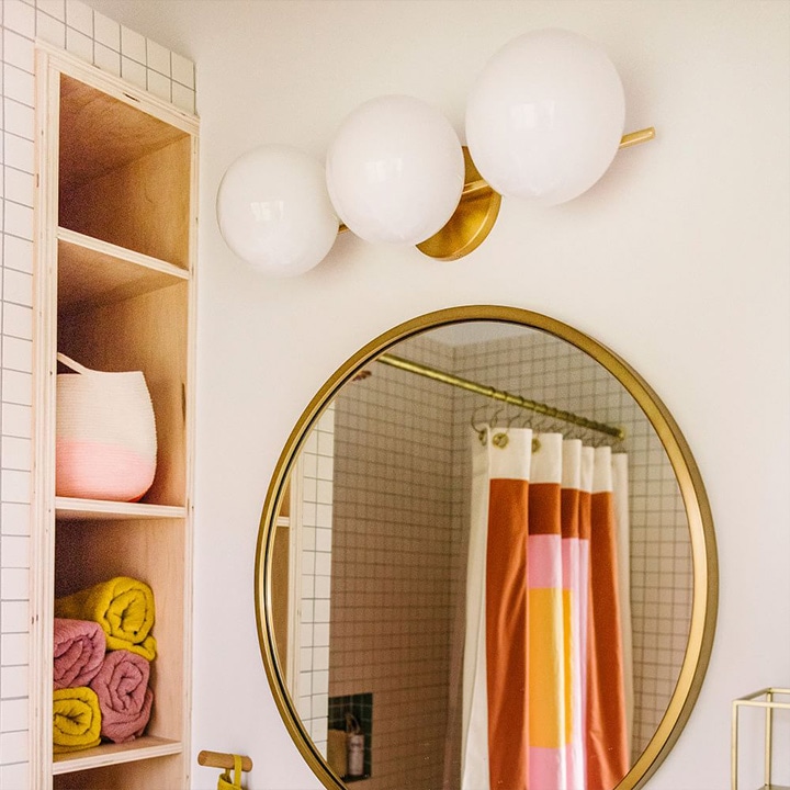 Three-light sconce above a round mirror in a bathroom.