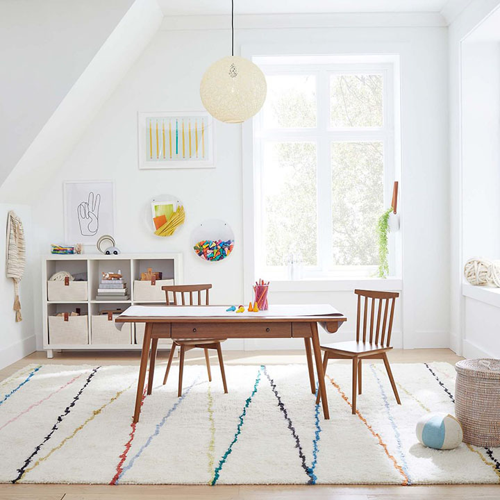 Dark wood craft table with rainbow area rug underneath in a kids playroom. 