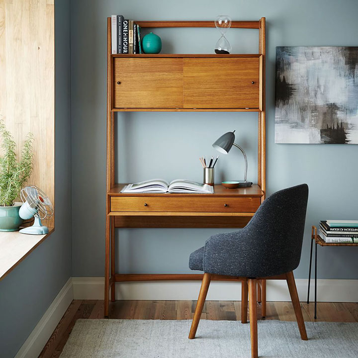 Wood module desk with matching desk chair next to small table and blue and black painting. 