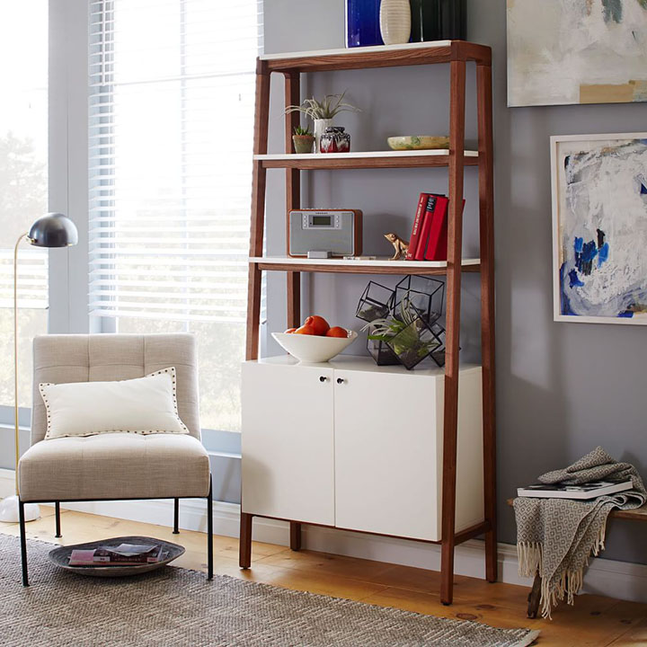 White accent chair with white pillow next to white and wood ladder bookcase in reading nook.