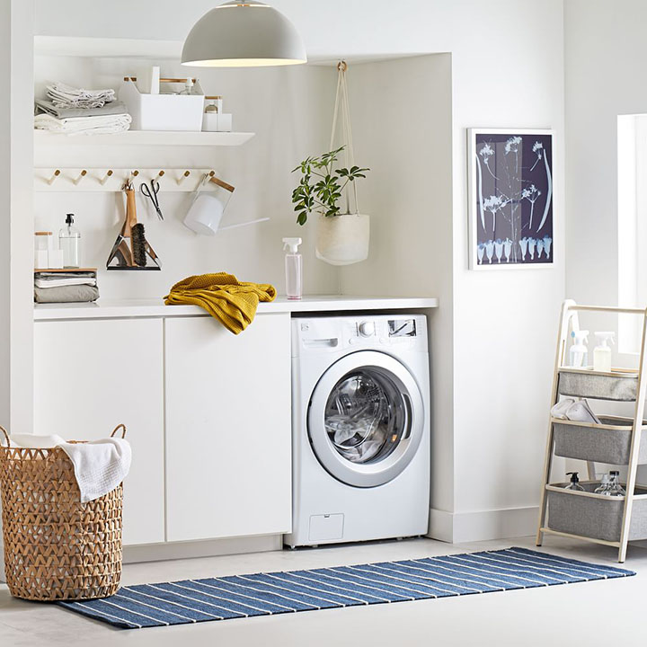 White washing machine in laundry room with blue striped rug and wicker laundry basket. 