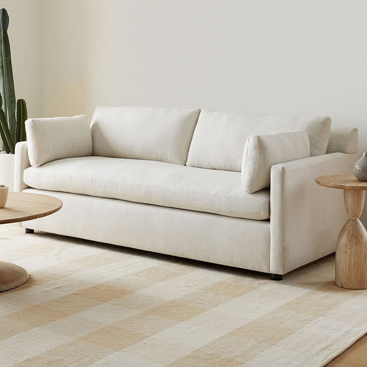 Beige loveseat with wood side table, coffee table and striped rug.