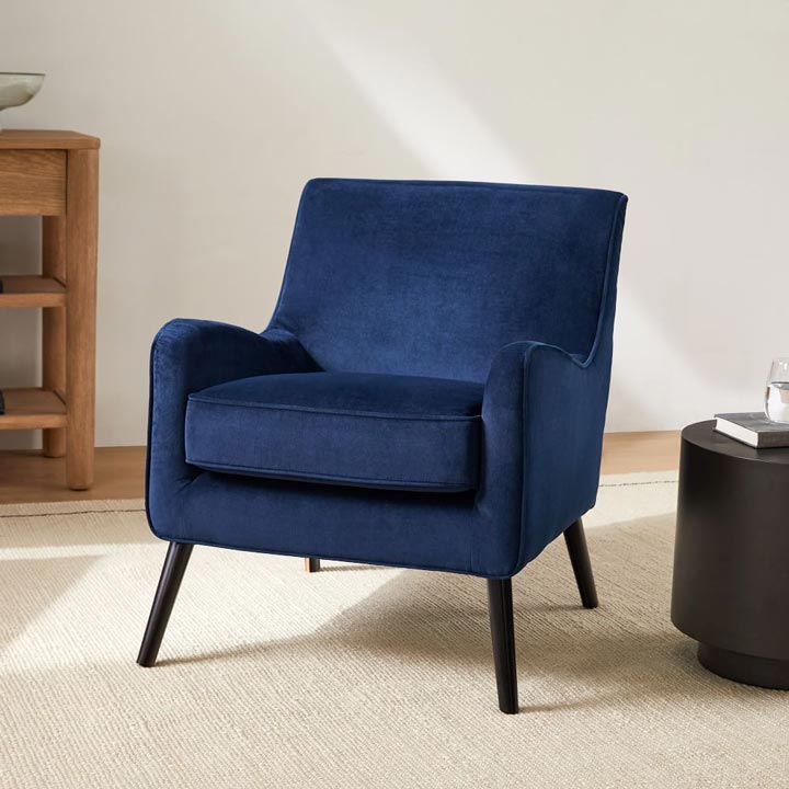 Navy blue accent chair styled with a neutral area rug and a black side table.