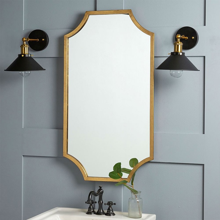 Two black and brass wall sconces on either side of a scalloped mirror.