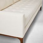 Close-up of front corner of tufted cream sofa showing leg and seat