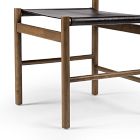 Front corner of a wooden dining chair with black leather seat and back, legs visible