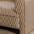 Close-up of the right arm and fabric pattern of a beige woven armchair.