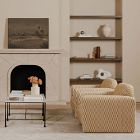 Living room scene featuring a beige woven armchair, a shelf with decor, and a small table with a toy-like figure.