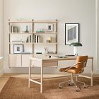 Modern light wood office desk with open shelving and a matching set of wall-mounted shelves, plus a leather chair and framed artwork.
