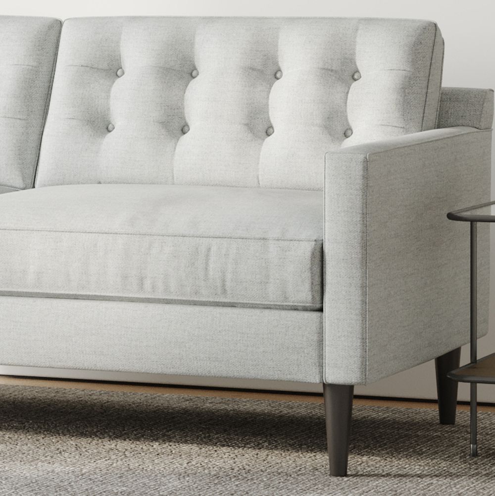 Light gray upholstered sofa with tufted back and wooden legs alongside a small round table