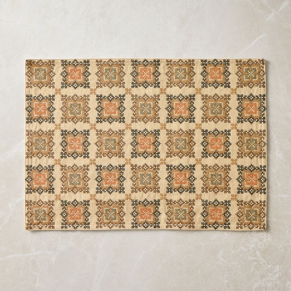 A woven placemat patterned with a grid of folk medallions in green, rust and coral