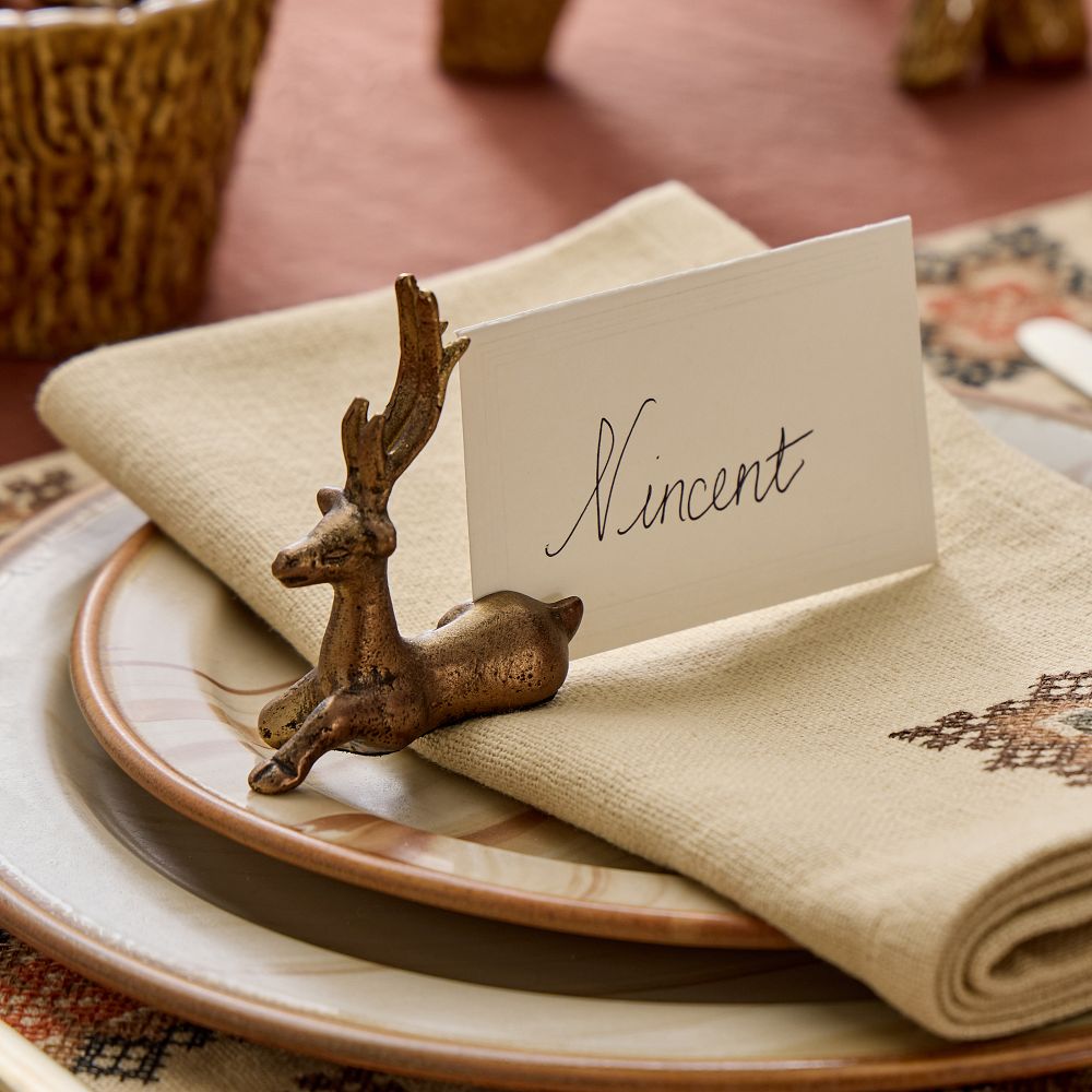 A small brass-finish deer holding a handwritten place card on a napkin