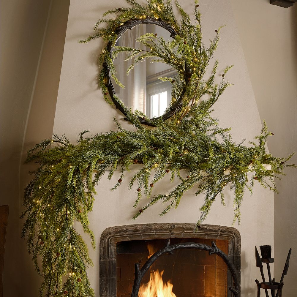 A long, loose garland of faux branches draped across a mantel above a lit fire