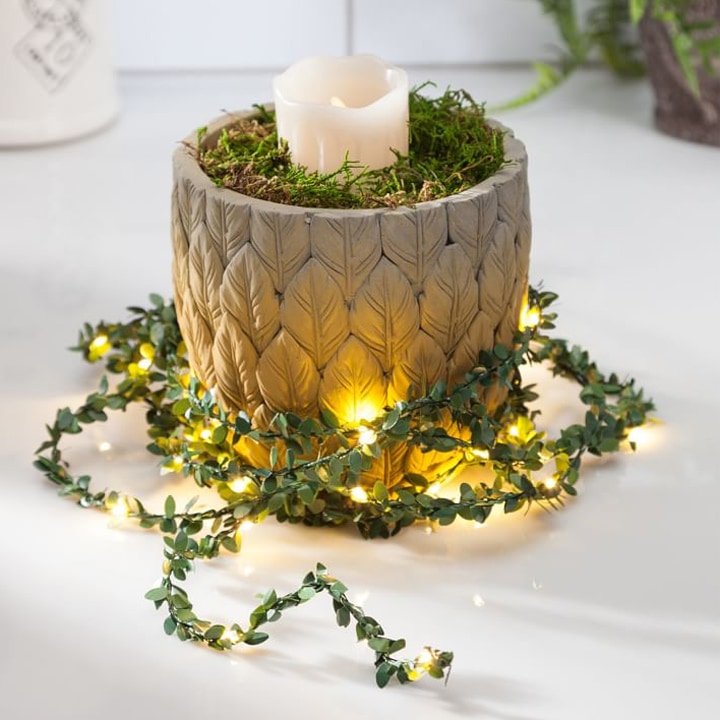 greenery and twinkle lights wrapped around concrete candle holder