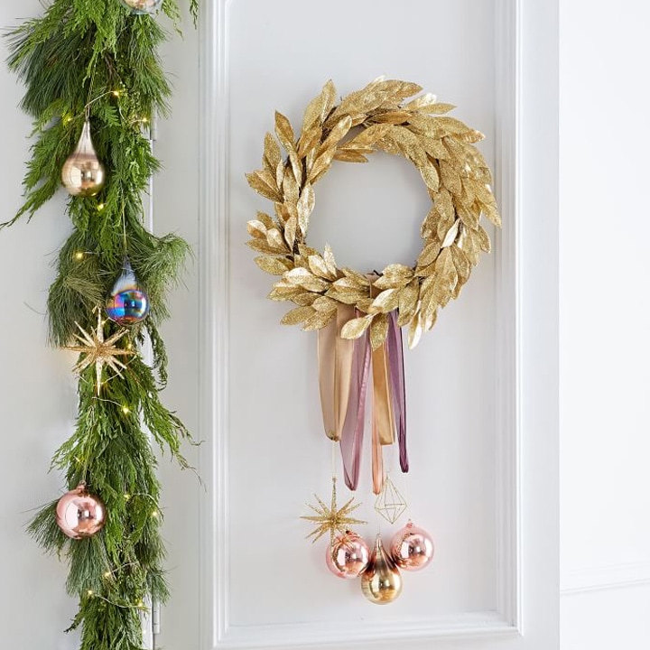 glittery gold wreath with ornaments and garland on white wall