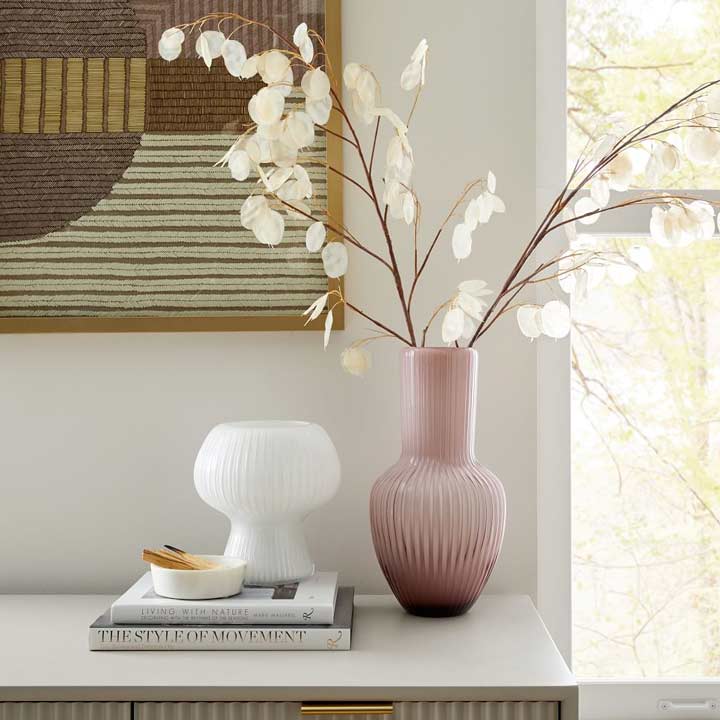 white and pink vase with faux flowers sitting on desk near window