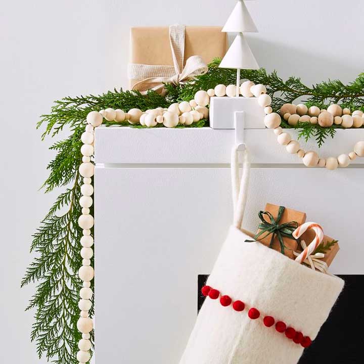 close up of green and wooden garland and white stocking on modern fireplace