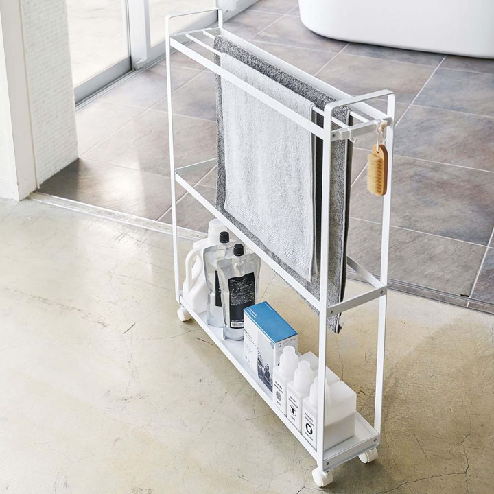 Narrow white rolling rack with towels and care products.