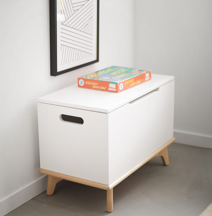 White toy chest with art on wall.